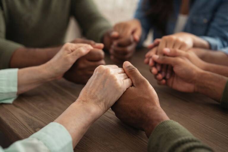 Hands joined together in prayer around a table